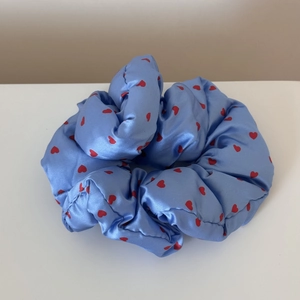 Detailed view of sky blue satin scrunchie with red heart patterns and smooth silk texture