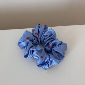 Close-up of light blue satin scrunchie with red heart patterns and silver brand tag