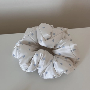 Detail of a creamy white satin scrunchie with light blue heart pattern and silky texture