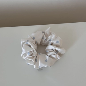 Detailed view of cream satin scrunchie with blue hearts and a silver round charm