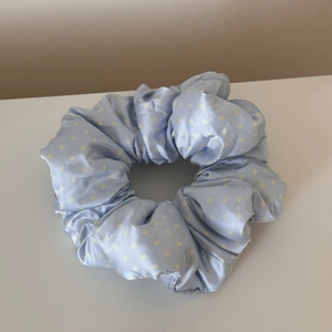 Detailed view of light blue satin scrunchie with white polka dots and soft texture