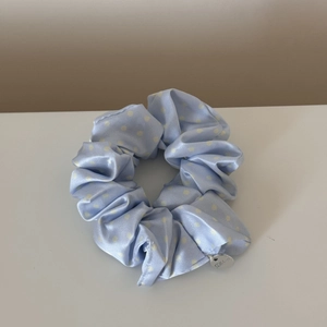 Detailed macro view of light blue satin scrunchie with white dots and silver metal tag