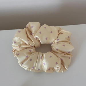 Detailed view of cream satin scrunchie with purple heart patterns and smooth texture