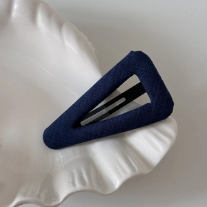 Detail view of navy blue polka dot fabric triangle hair clip on a white shell plate