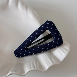 Detailed macro view of the navy blue polka dot fabric triangular snap hair clip on a dish