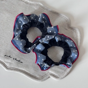 Close-up of two light blue polka dot scrunchies with red edges on a gray tray