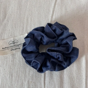 Gros plan d'un chouchou en denim bleu foncé avec des plis en tissu et une petite étiquette