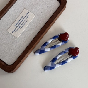 Detailed view of two blue and white gingham fabric hair clips with red heart accents