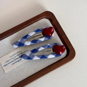 Detail showing two blue and white checkered hair clips with a red heart in a tray