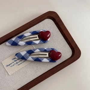 Close-up of blue and white checkered fabric hair clips with red 3D heart charms on a tray