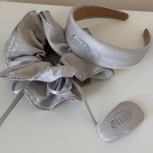 Vue macro d'un chouchou et bandeau en satin gris argenté avec broderie de marque