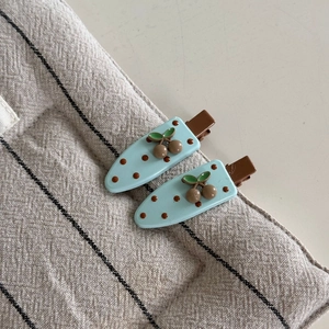 Vue détaillée des barrettes bleu clair avec motifs de cerises brunes et de pois mignons