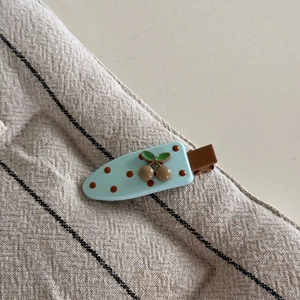 Vue détaillée d'une pince à cheveux cerise bleu clair à pois marrons sur tissu rayé