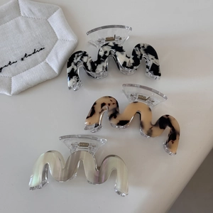 Three wave-shaped acetate hair claw clips in tortoise shell and marble patterns