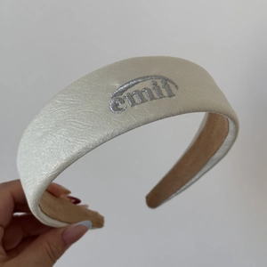 Gros plan sur un serre-tête en similicuir crème avec logo brodé argenté et doublure douce