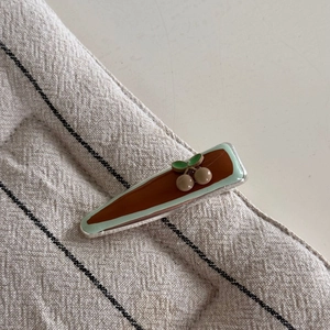 Détail d'une pince à cheveux vert menthe avec motif cerise sur fond en tissu rustique