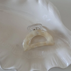 Close-up of a semi-circular acetate hair claw clip with marble texture on a shell tray
