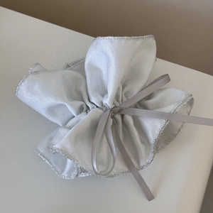 Détail du pochon cadeau argenté métallisé avec ruban satiné et bords à froufrous