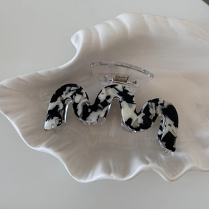 Macro detail of wave-shaped marble pattern acetate hair claw clip on a white shell tray