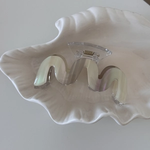Close-up of a wavy iridescent hair claw clip with golden metal spring on a shell tray