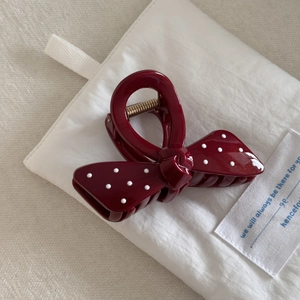 Detail of burgundy polka dot hair claw clip with gold spring on white fabric