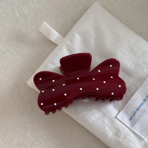 Macro shot of a wine red polka dot hair claw clip resting on a white fabric pouch