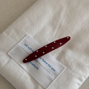 Detail der weinroten Polka-Dot-Haarklammer mit glänzender Optik auf weißem Stoff