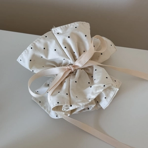 Detailed view of beige drawstring pouch with black polka dots and pink satin ribbon tie