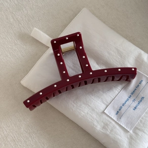 Detail of burgundy polka dot hair claw clip with golden spring on white fabric