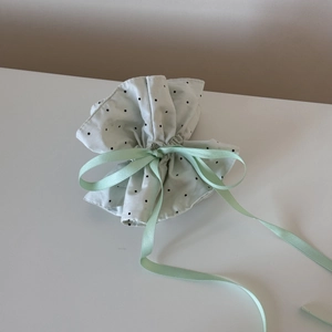 Close-up of a white polka dot drawstring pouch with a soft green satin ribbon bow