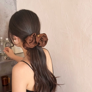 Brown silk scrunchie with gold accent on low ponytail in a retro aesthetic scene