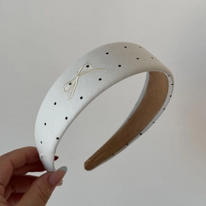 Detail of white satin headband with black polka dots and embroidered bow decoration