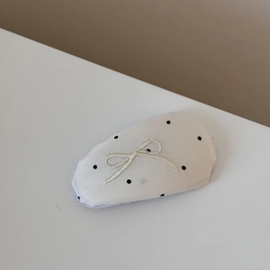 Detailed close-up of a white polka dot hair clip with beige embroidered bow detail