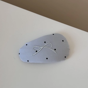 Close-up of light blue fabric hair clip with black polka dots and grey bow embroidery