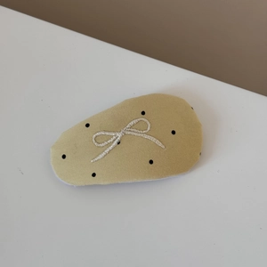 Detail of yellow polka dot fabric hair tie featuring a delicate white embroidered bow
