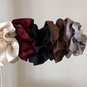 Detail of five oversized pleated satin scrunchies in cream, red, black, coffee, and violet