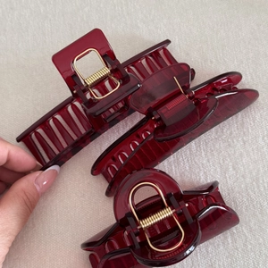 Three deep red translucent hair claws with gold springs and tortoiseshell texture details
