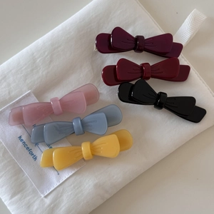 Detail of six colorful acetate double-layered bow hair clips on a white fabric bag