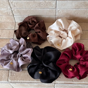 Detailed close-up of premium satin scrunchies with elegant gold round metallic emblems