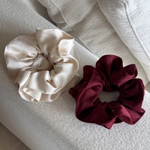 Detail of premium satin scrunchies in cream and burgundy with gold logo charms