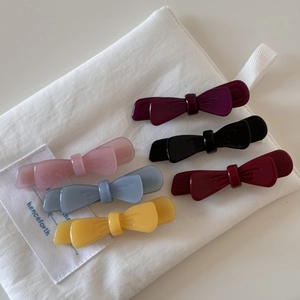 Detail of six colorful acetate double-layered bow hair clips on a canvas pouch