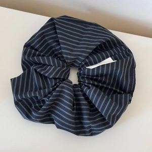 Detail of blue striped scrunchie with fine pleats and white fabric label on white background