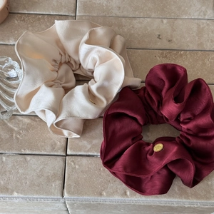 Macro detail of silk satin scrunchies with elegant folds and gold metal logo charm