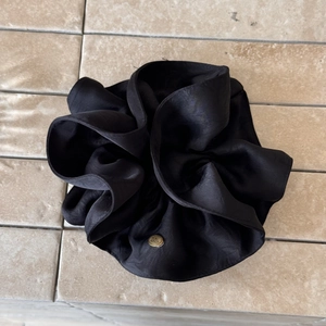 Detail of black silk satin scrunchie featuring a premium gold oval metal brand logo tag