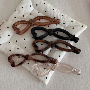 Detail showing five different colors of bow-shaped resin banana hair clips on a dotted fabric