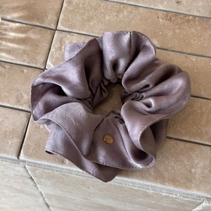 Detailed macro view of purple silk satin scrunchie with golden oval metal brand tag