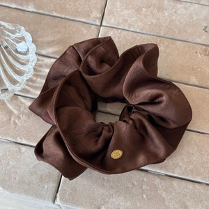 Macro shot of dark brown ruched fabric scrunchie with an oval gold metal logo tag