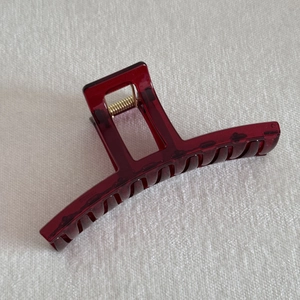 Detail of a dark red rectangular hair claw clip with a glossy finish and metal spring