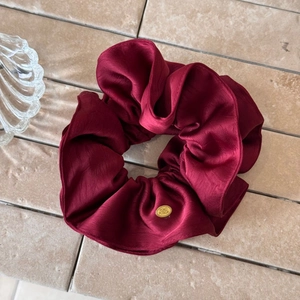 Macro shot of burgundy satin scrunchie with shiny texture and golden oval metal tag