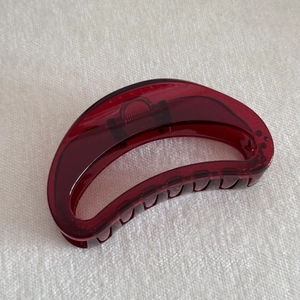 Close-up of translucent red minimalist hair claw clip with silver metal spring on white fabric